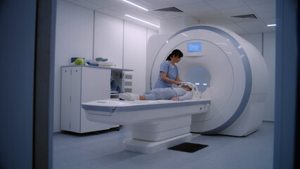 Female doctor, radiologist controls and turns on MRI or CT scan machine for female patient. Caucasian woman undergoing cancer prevention check up in modern clinic with advanced medical technologies.