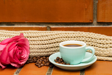 Brick background, blue mug with coffee, pink rose.
