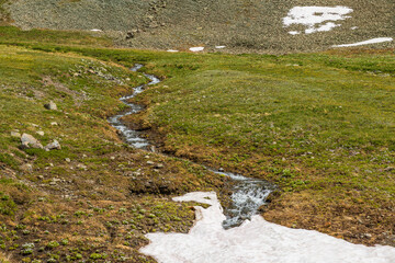 Fototapeta na wymiar mountain river flowing through tundra meadow into snowfield