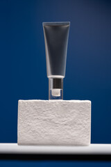 Silver metal cosmetic tube on white stone stage, blue background, mock up, make up. Minimalist...