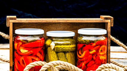 Wooden crate with glass jars with pickled red bell peppers and pickled cucumbers (pickles)...