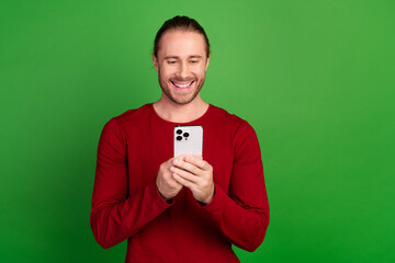 Portrait of smart clever guy with long hair wear red shirt choose product in eshop on smartphone isolated on green color background