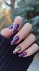 Hand displaying winter French manicure with dark lilac and gold nails, against a soft-focused Christmas tree background.