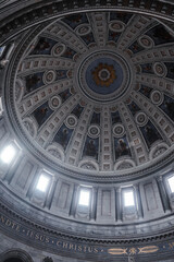 Captivating interior of a grand domed cathedral with Latin inscriptions, radiant centerpieces, and statues in niches, bathed in natural light from large windows. Location unspecified.