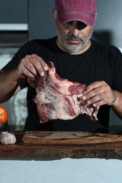 Hombre condimenta carne. Hombre prepara asado. Hombre latino prepara comida casera. Concepto de comida realizada en casa. Asado argentino.  Hombre corta papas. Hombre prepara una comida.