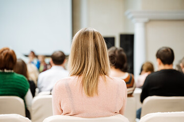 Blonde woman in pink sweater sitting in conference room with audience