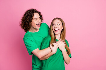 Portrait of couple laughing friends have fun together buddies at party wear same green t shirt isolated over pink color background