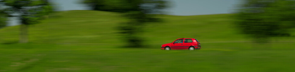 A red Volkswagen Golf drives through a green landscape, Bayersoien, Bavaria, Germany