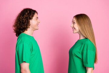 Profile side photo of happy couple teenagers smiling girlfriend blonde looking at brunet curls boyfriend isolated on pink color background