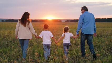 Happy family walks holding hands in park sunset. Children, parents relax carefree. Family walks on green grass with flowers. Family travel parents daughter son. People traveling outdoor. Happy people