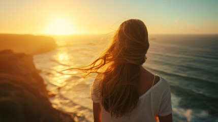 Fototapeta premium powerful woman standing on a cliff overlooking the ocean at sunrise, her hair flowing in the wind, symbolizing strength and freedom