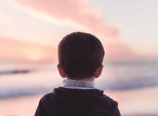 Child looking to the sea. Unrecognizable boy staring to the ocean on the beach at beautiful pink sunset. Travel on summer.