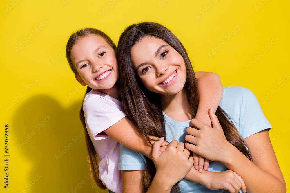 Poster photo of pretty shiny little sisters wear t-shirts cuddling smiling empty space isolated yellow colo