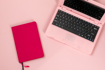 Pink laptop with pink notebook on pink background, feminine workplace