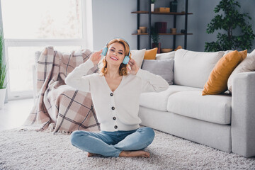 Full body portrait of pretty positive lady sit barefoot carpet floor hands touch headphones pastime chill house indoors