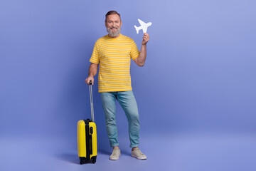 Full length photo of positive aged man hold suitcase paper plane empty space isolated on violet color background