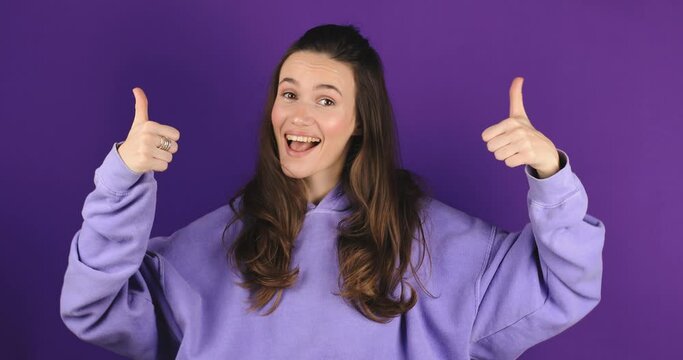 Young woman in violet hoody making good-bad sign isolated on purple background. Girl make choice, or makes a decision thumb up or thumb down, like or dislike, yes or no.
