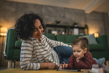 Mother and daughter use digital tablet to watch online video at home