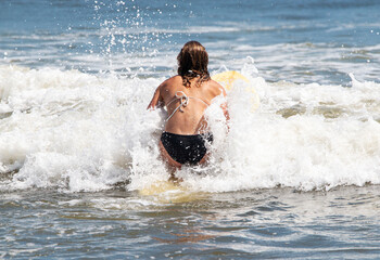 Fototapeta premium Girl in a bikini on her knees on a surfboard trying to paddle out past the surf