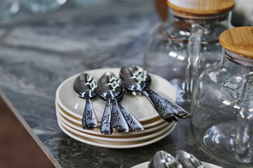 A stack of white porcelain plates and tea spoons on top, On the buffet table.