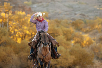 Cowgirl riding horse holding onto hat