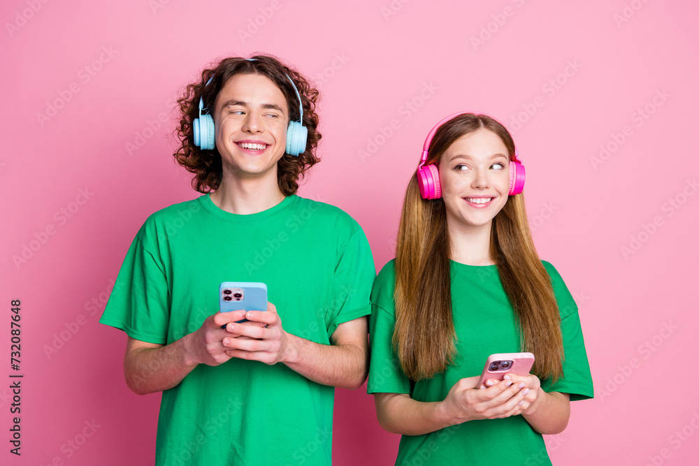 Sticker Photo of looking each other couple geek teenagers hold cell phones enjoy earphones with nice quality music isolated on pink color background