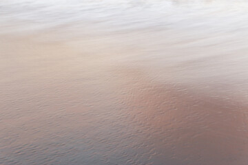 Blurred flat surface sea water on pastel orange beach sand natural background