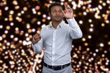 Young attractive indian businessman working on invisible interface. Festive bokeh lights in the...