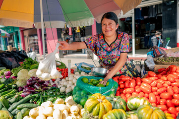 Portrait of indigenous woman watching Camara at her fruit and vegetable stall in a local market.