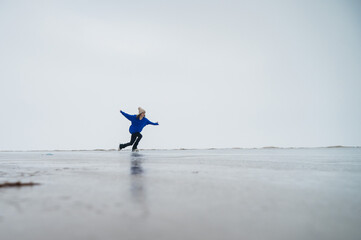 Caucasian woman in a blue sweater is skating on a frozen lake. The figure skater performs the program.