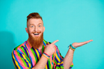 Photo of optimistic smile red hair funny guy hipster in lgbt shirt holding arm pointing finger barbershop isolated on cyan color background