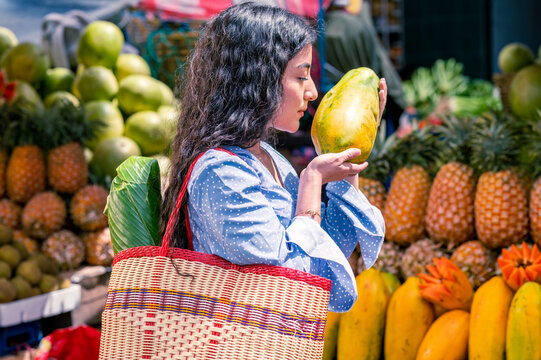 Close-up of a Latin girl in the middle of a fresh fruit market, with a basket holding a papaya in her hands.