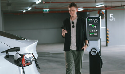 Young man travel with EV electric car to shopping center parking lot charging in downtown city...