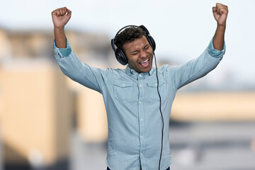 Energetic young man listening to music with headphones and raised his hands. Positive emotions from...