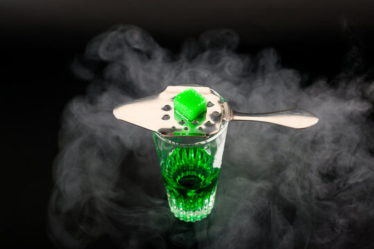Green flavoured vodka called Absinthe served in a shot glass with a special spoon with white sugar cubes