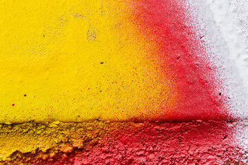 Macro close-up of a wall spray painted with bright yellow, red and white. Abstract full frame textured splattered and colorful graffiti background with copy space.