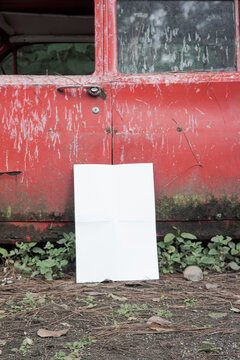 white blank poster for mockup on a damaged car in an abandoned forest, red background, potrait 1