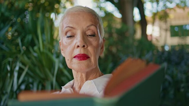 Mature lady looking book in green garden closeup. Stylish senior enjoying hobby