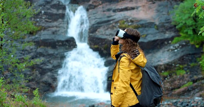 Woman, vr and waterfall for metaverse, nature and adventure in forest for fitness simulation. Female, adventure and tech in outdoor scenery, headset and virtual reality escape city with hike