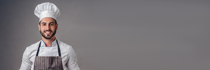 Naklejka premium Panoramic portrait of male chef in apron and hat, isolated on grey background with large copy space for text