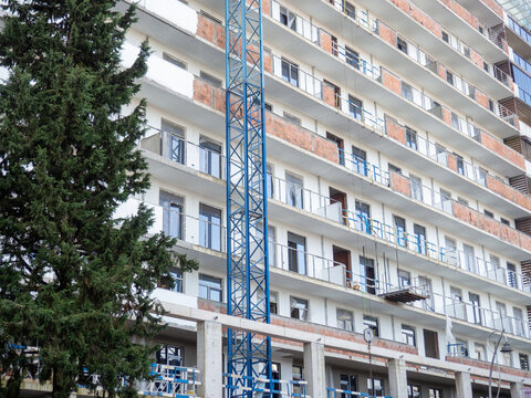 facade of an unfinished high-rise building. Construction crane near a panel house.