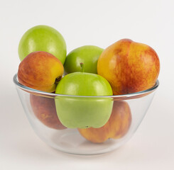 Close-up of green apples and nectarines in a glass bowl on a white background. Concept of healthy food in summer.
