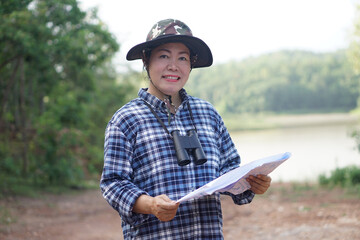 Asian woman explorer hold paper map to explore nature at forest and lake area. Concept, nature...