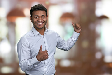 Cheerful guy pointing on copy space behind his back. Indian man pointing with thumb at copy space....