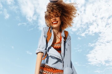 Smiling Woman in Beach Lifestyle, Dancing with Open Mouth in Happy Hippie Style, Enjoying Freedom and Nature: Portrait of a Young Model in Curly Hair, Under Wide Angle Lens, during Fun-filled Summer - obrazy, fototapety, plakaty