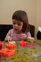 Four-year-old girl in a striped shirt making holiday cookies at home. She is shaping cookie dough with cutters, preparing baking trays, and enjoying a fun and creative kitchen activity. Concept of chi