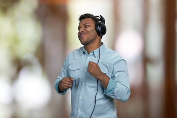 Relaxed indian man enjoying listening to music with headphones. Interior blur background.
