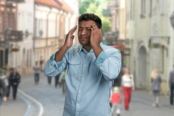 Tired indian man suffering from headache standing outdoors. Health problem concept.