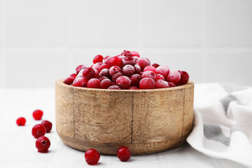 Frozen red cranberries in bowl on white tiled table, closeup