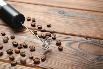 Black milk frother wand and coffee beans on wooden table, closeup. Space for text